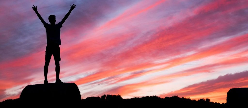 silhouette of a man celebrating at sunset