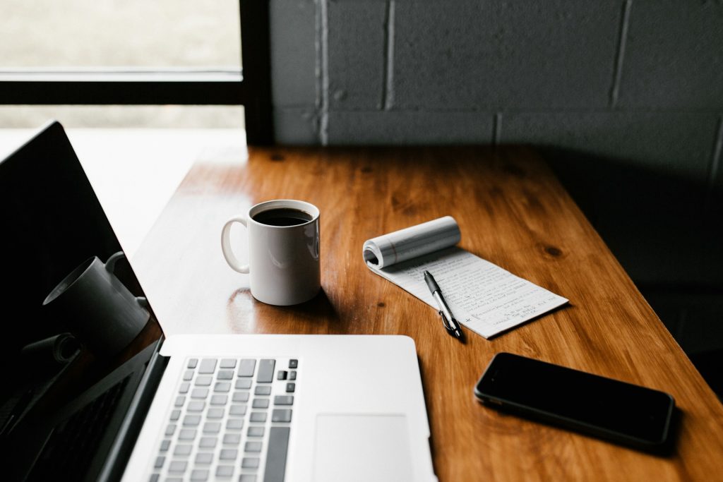 a lap top, cup of coffee, and notebook on a desk