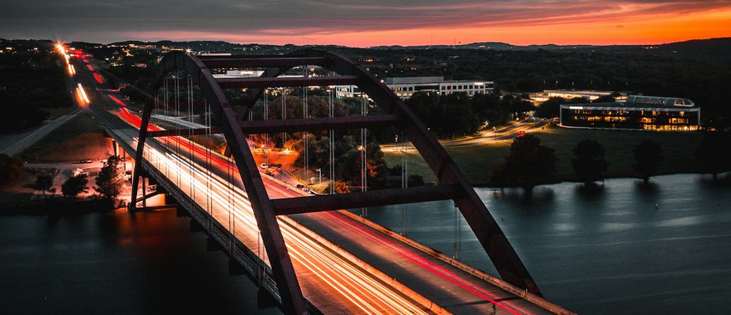 blurred vehicle lights racing over a bridge at dusk