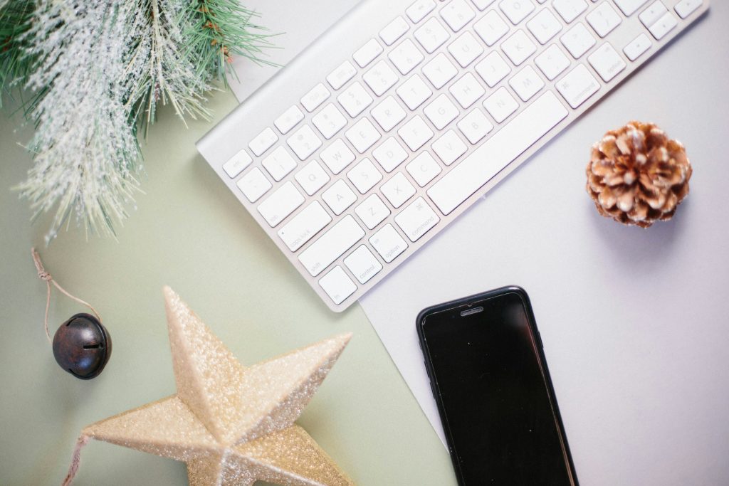 a keyboard next to a pine cone, an evergreen branch, a star, and a Christmas ornament 