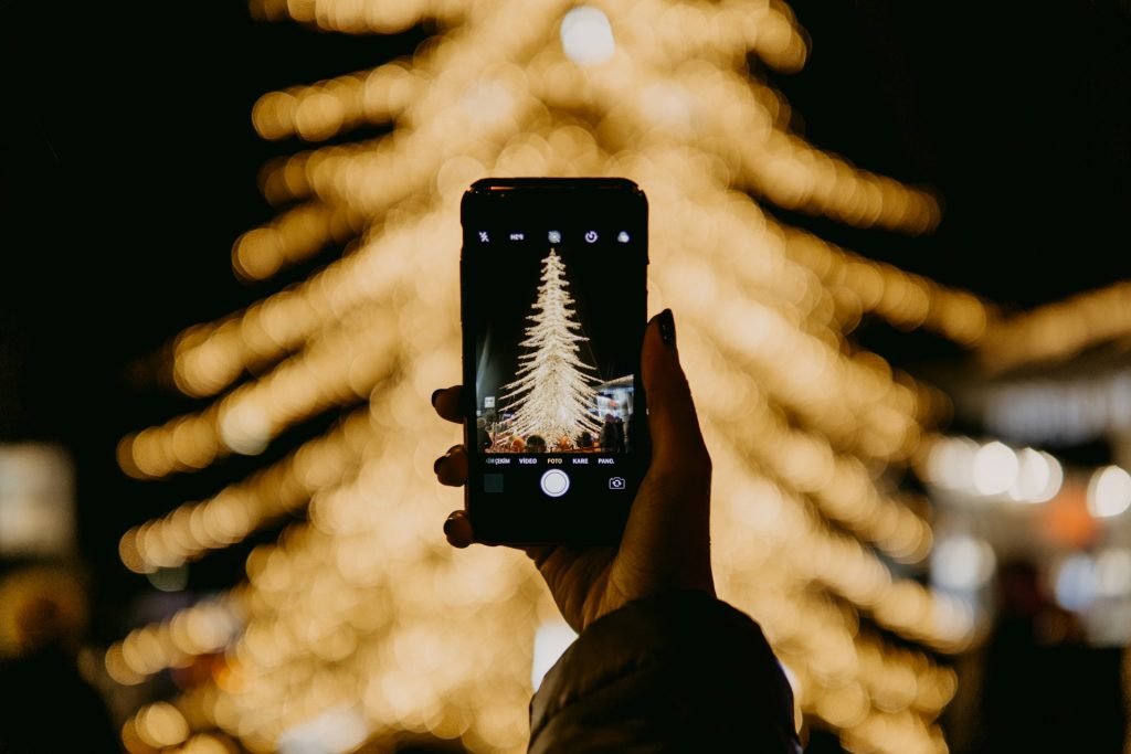 hand holding up a phone to take a photo of a Christmas tree